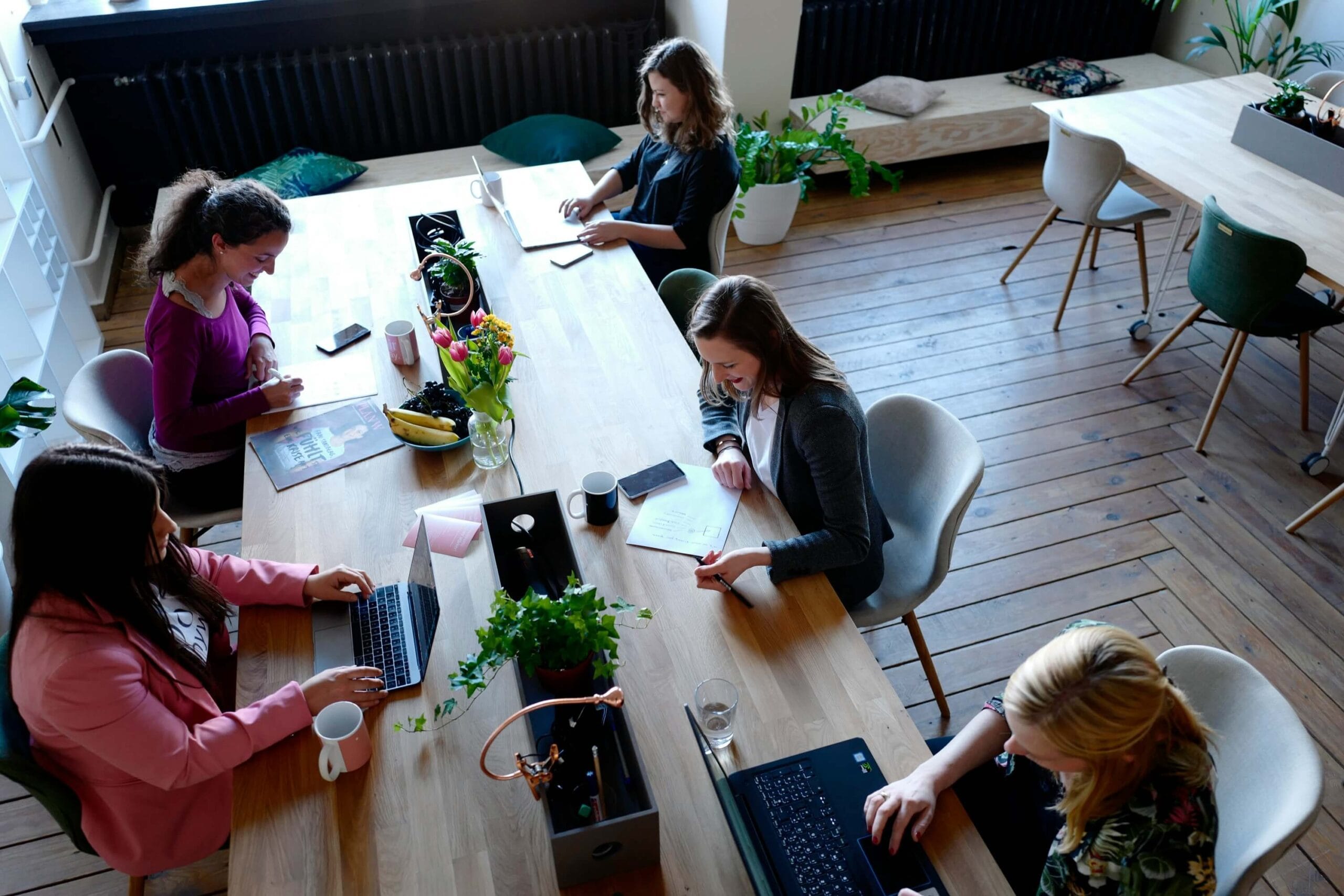 Group of 5 women sitting around a rectangle desk coworking